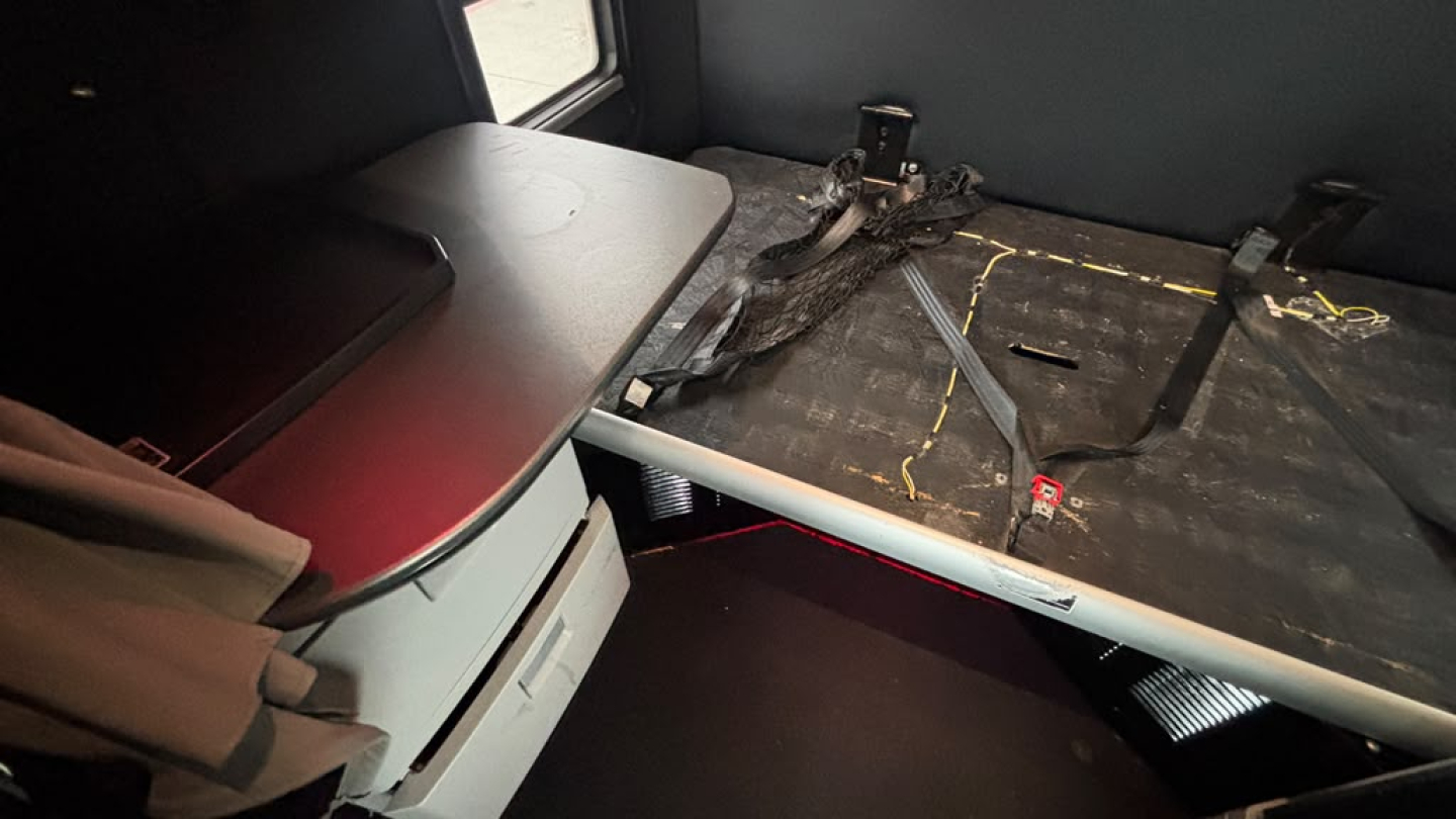 Interior sleeper area of a 2024 Kenworth T680 with a flat desk/table and seat belt anchors visible on a textured sleeper platform.