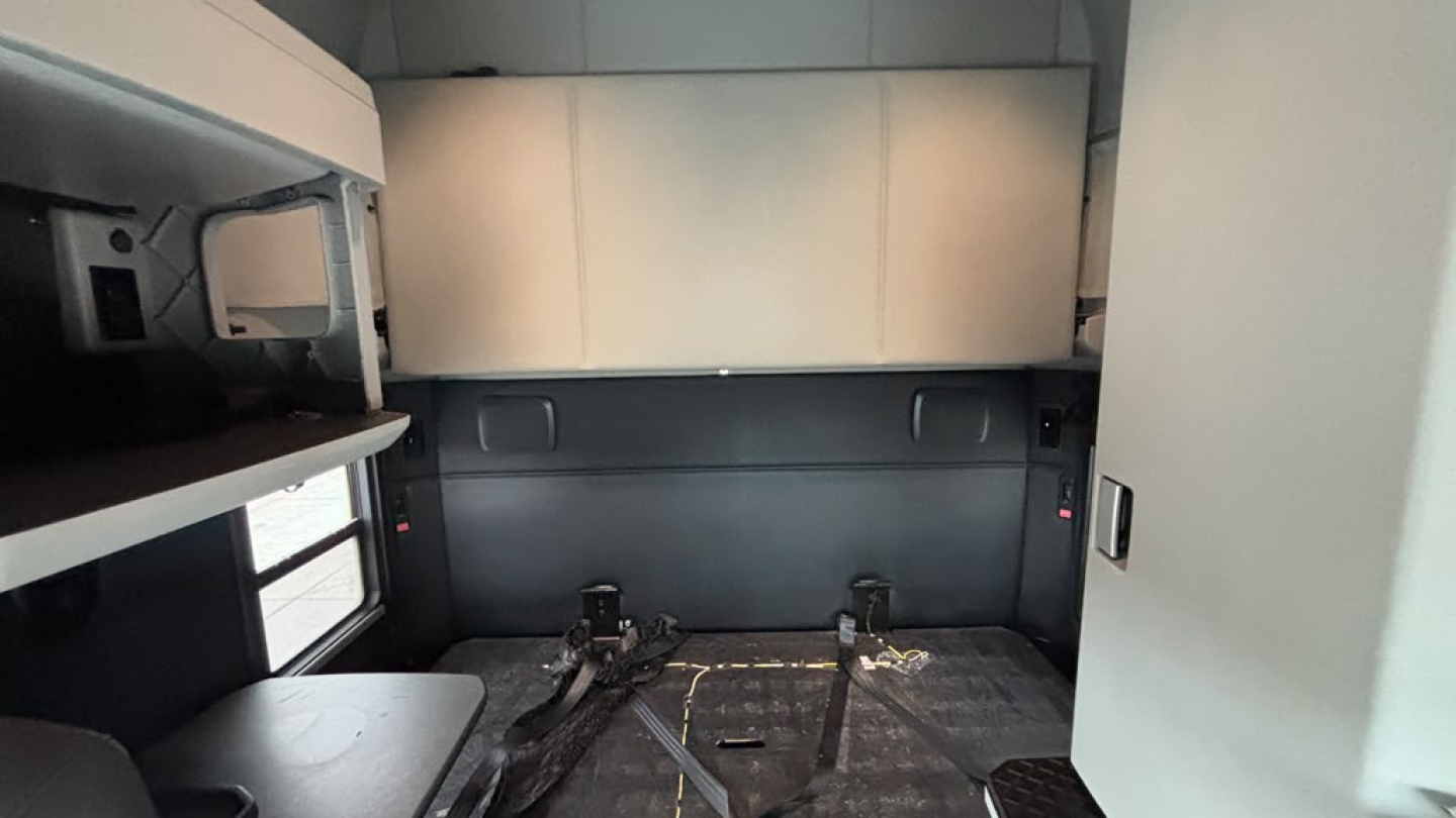 Kenworth T680 interior sleeper cab cargo area with empty floor and storage cabinets visible, side windows and bunk framework