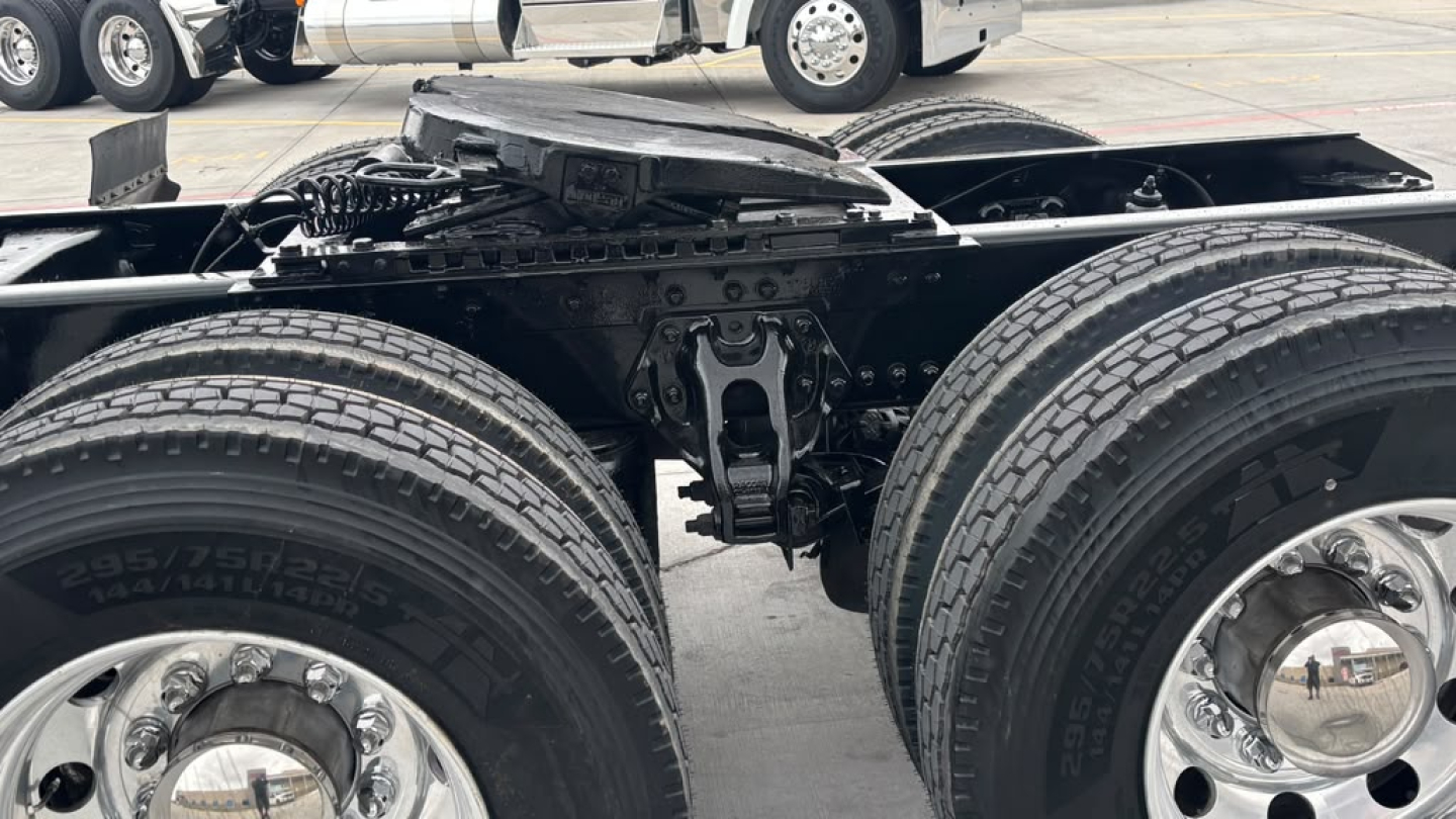 Kenworth truck undercarriage showing dual rear axles and suspension components with tires and chrome hubs.