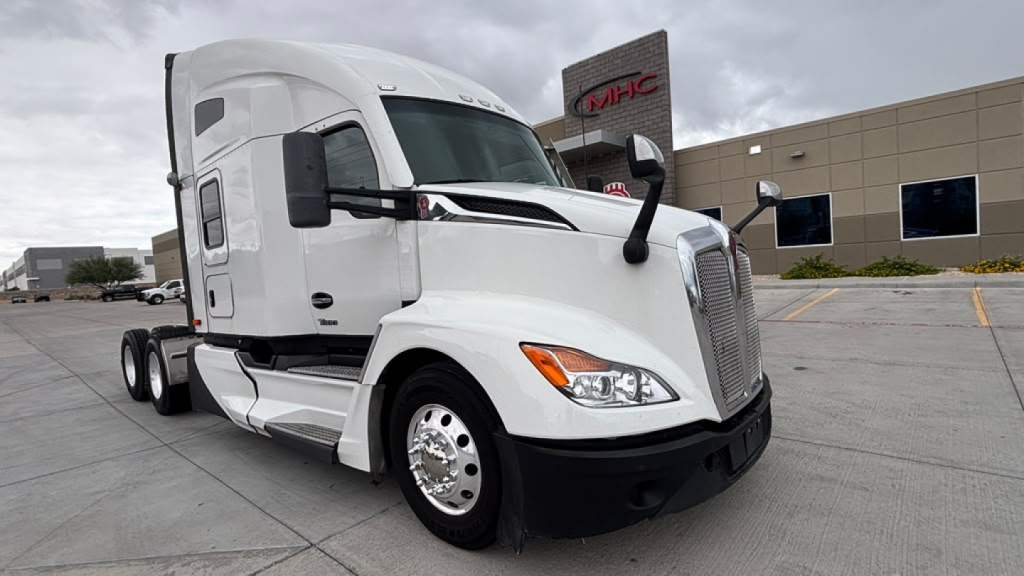 Kenworth T680 front-left view showing cab and chrome wheels, with a dealership building in the background.