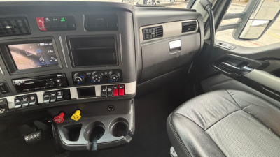 Kenworth T680 cab interior view showing dashboard, steering column, and driver seat; visible controls and touchscreen left of center, air vents, cup holders.