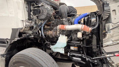 Kenworth T680 engine bay view showing cooling reservoir, hoses, turbo intake, and various engine components in a truck. Visible label areas and wiring harnesses.