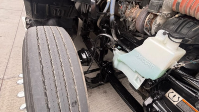 Kenworth T680 engine bay and front wheel showing coolant reservoir and engine components.