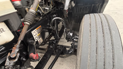 Kenworth T680 engine bay area showing front suspension and steering components, visible hoses and wiring, and a single front tire with tread.