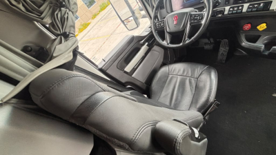 Vehicle interior showing driver's seat and steering wheel of a Kenworth truck cab with dashboard controls visible.