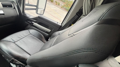 Seat and interior of a Kenworth truck cabin with black leather seat in view, armrest and window controls visible.