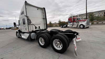 Truck chassis and rear section of a 2024 Kenworth T680, semi-truck with sleeper cab, showing dual rear axles and fifth wheel mounting, exterior white paint.