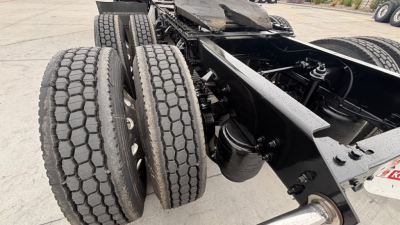 Dual rear axles and suspension of a Kenworth truck chassis showing twin tires and leaf spring components with a portion of undercarriage and frame.