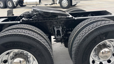 Kenworth truck undercarriage showing dual rear axles and suspension components with tires and chrome hubs.