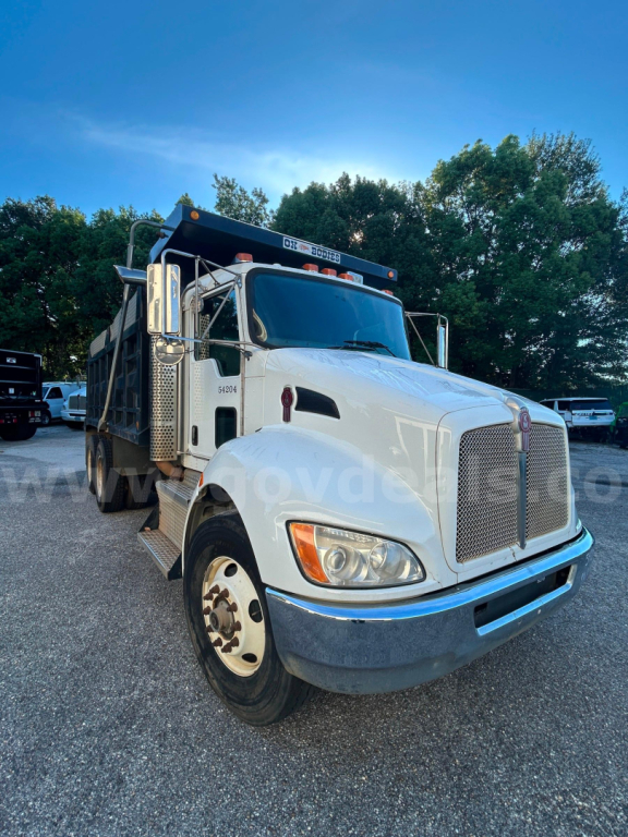 Kenworth T370 dump truck front-left view showing grille, headlights, side mirrors, and dump bed; white cab with chrome grille and black dump bed top rail.