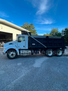 Kenworth T370 dump truck side view showing dump bed and hydraulic hoist with cab, chrome wheels, and blue exterior.