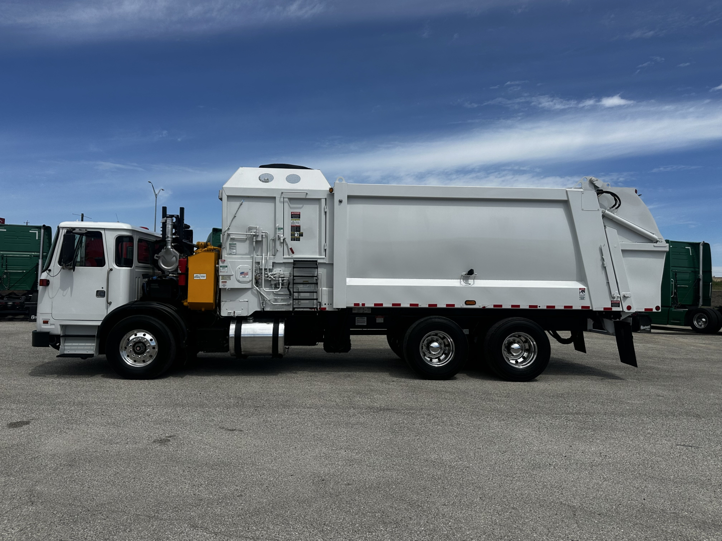 Autocar XPEDITOR truck side view showing large rear compactor body and cab, white with black chassis and wheels, clear blue sky.