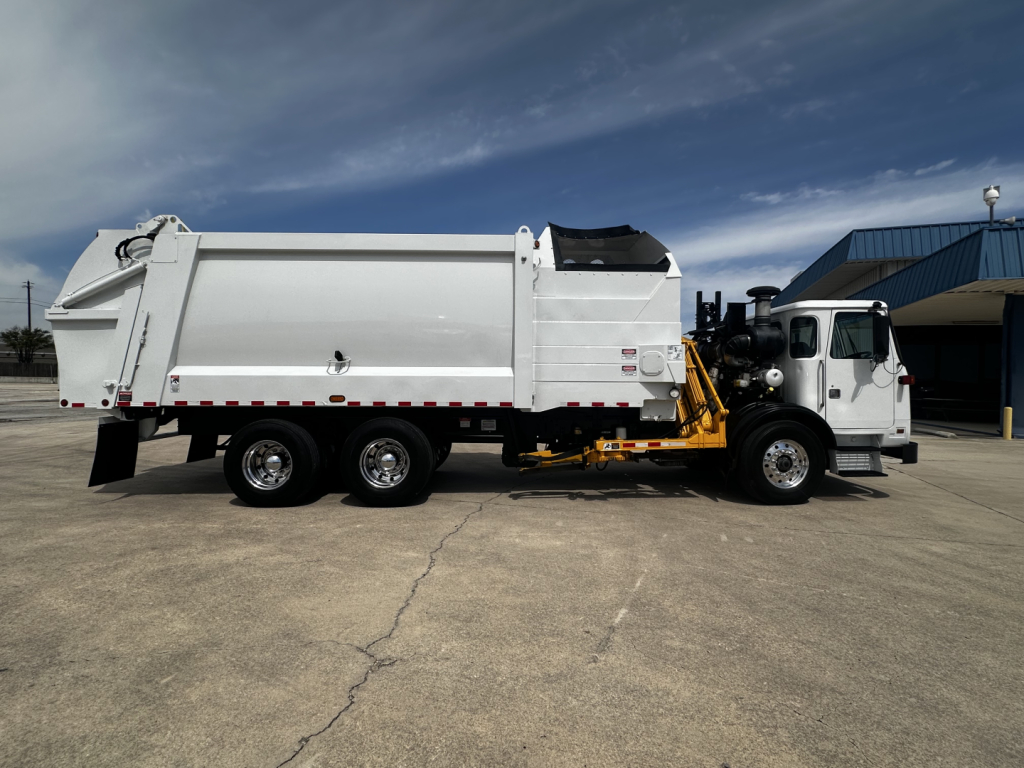 Autocar XPEDITOR truck in side view showing large dump bed and hydraulic arm, white cab, three rear axles, black exhaust stack, and yellow mechanism.