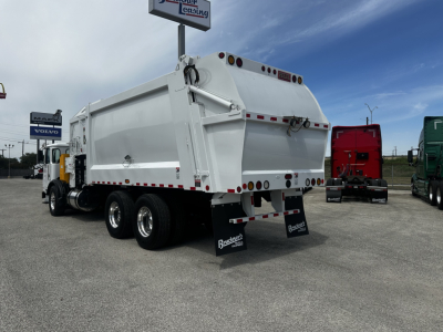 Rear and side view of a 2019 Autocar XPEDITOR dump truck in a dealership lot, white cargo bed, multiple axles, black mudflaps with 'Bailey' branding, other trucks in background.