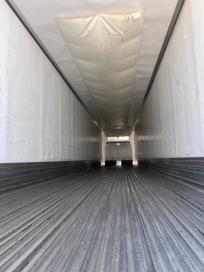 Inside view of a 2022 Utility 3000R trailer with ribbed metal floor and white interior, rear shows utility refrigeration unit and door.