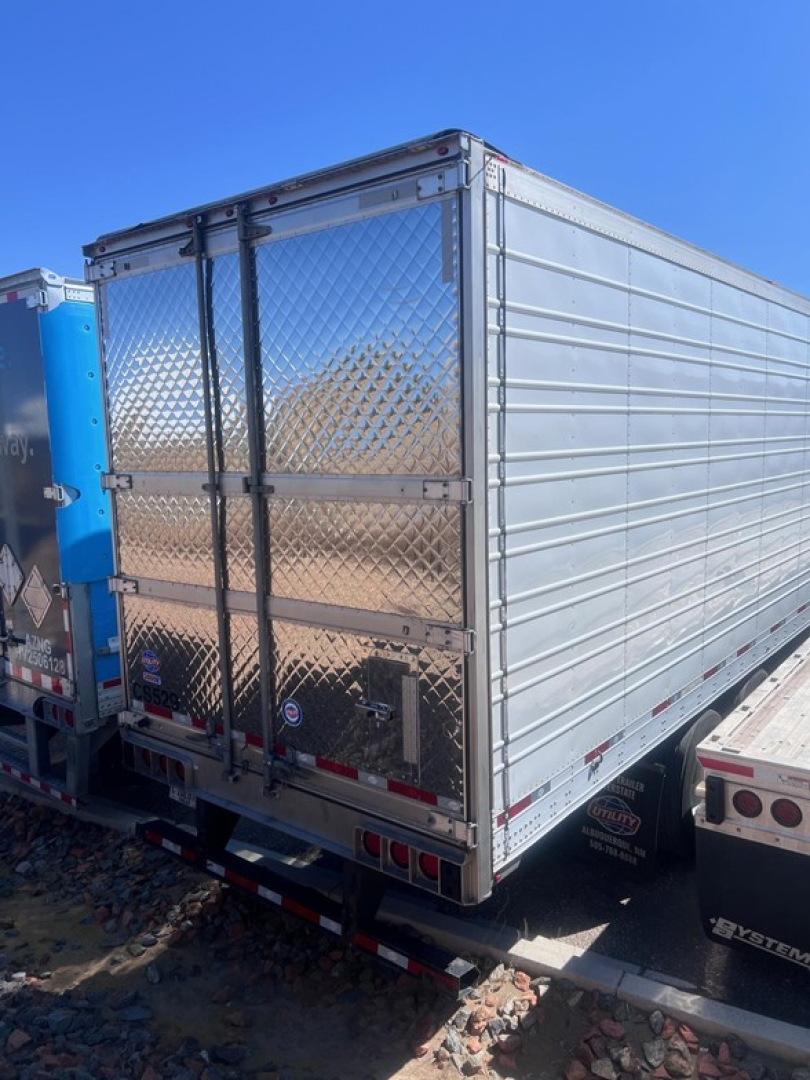 Trailer rear view of a silver diamond-plate utility trailer with double doors showing metal latch hinges and safety lights.