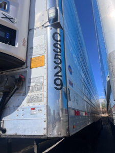 Truck trailer side with CS5029R and various warning labels; chrome metal surface; vertical CS5029R text; some small stickers and panels near the front of the trailer.