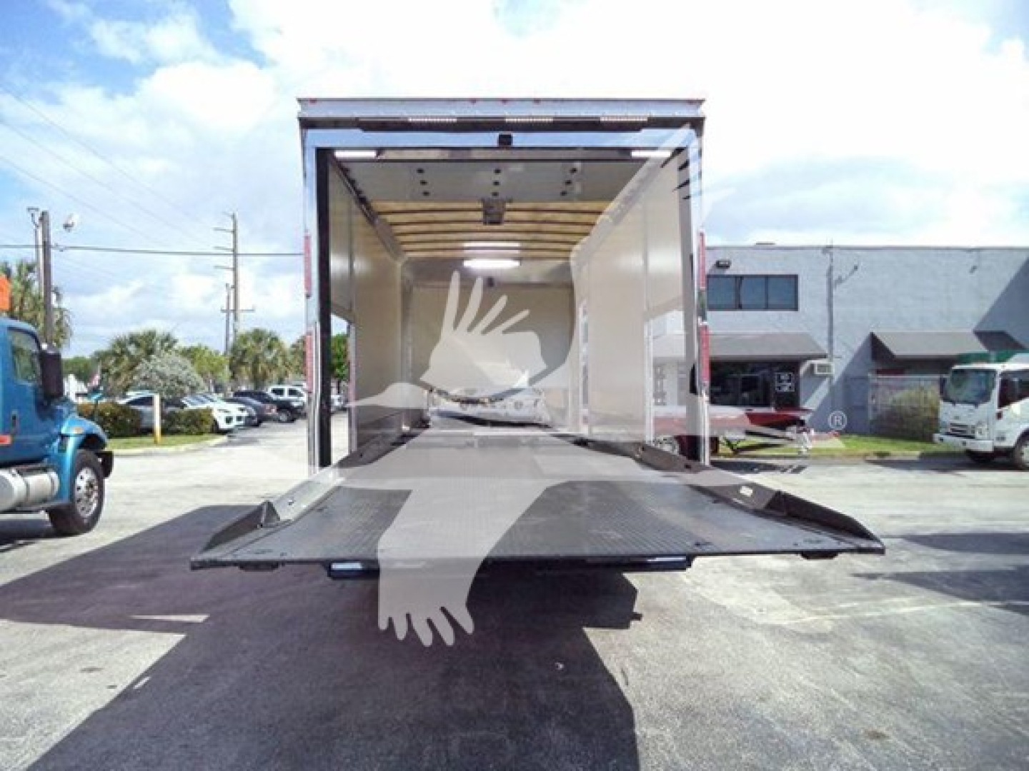 Truck cargo bed open with ramp down and loading area visible; rear of 2022 Mack MD6 rollback truck and oblique view of surrounding area.