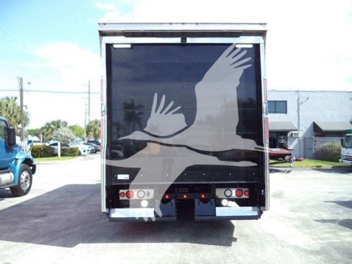 Rear view of a Mack MD6 rollback truck trailer with a large graphic of birds on the back doors and taillights visible.