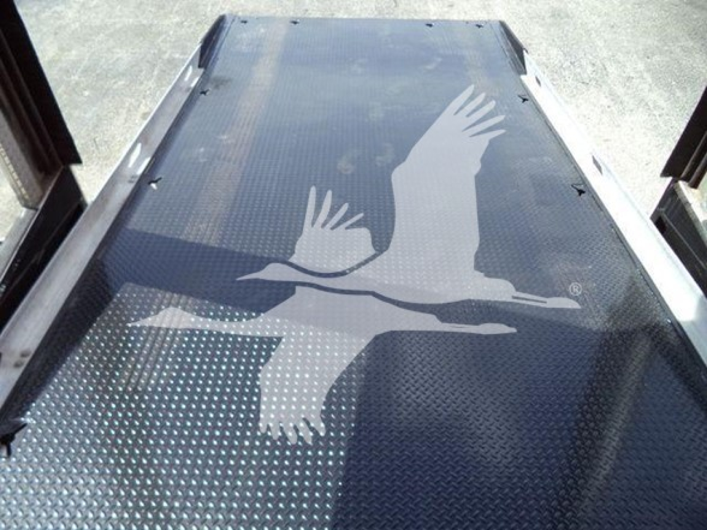 Truck flatbed with textured metal deck featuring a large white seagull graphic. Side rails and ramp edges are visible.