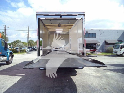Truck cargo bed open with ramp down and loading area visible; rear of 2022 Mack MD6 rollback truck and oblique view of surrounding area.