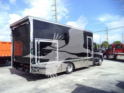 Truck body showing a matte black and chrome Mercedes-style utility trailer with rear access ramp and side door, in a dealership lot.