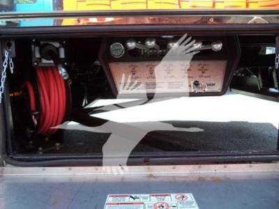 Rear-of-truck storage bay showing control panel with gauges and hoses, Mack MD6 rollback equipment visible