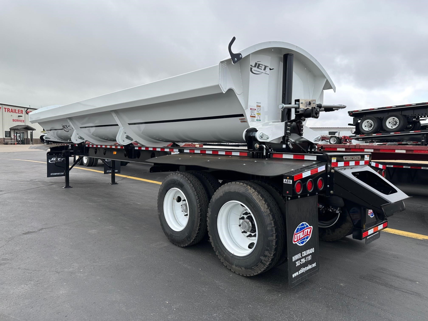 Jet side dump trailer on a flatbed trailer showing Jet logo on the side and dual rear wheels with mud flaps.