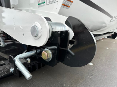 Dump trailer hitch and auger-looking blade on side dump trailer showing hitch pin and safety components.