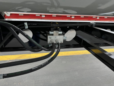 Equipment image showing hydraulic hoses and valve assembly under a jet side-dump trailer, with metal frame and piping visible.