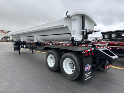 Jet side dump trailer on a flatbed trailer showing Jet logo on the side and dual rear wheels with mud flaps.