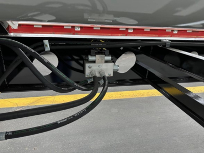Trailer undercarriage showing hydraulic lines and actuator assembly for a Jet side dump trailer, with metal brackets and hoses visible.