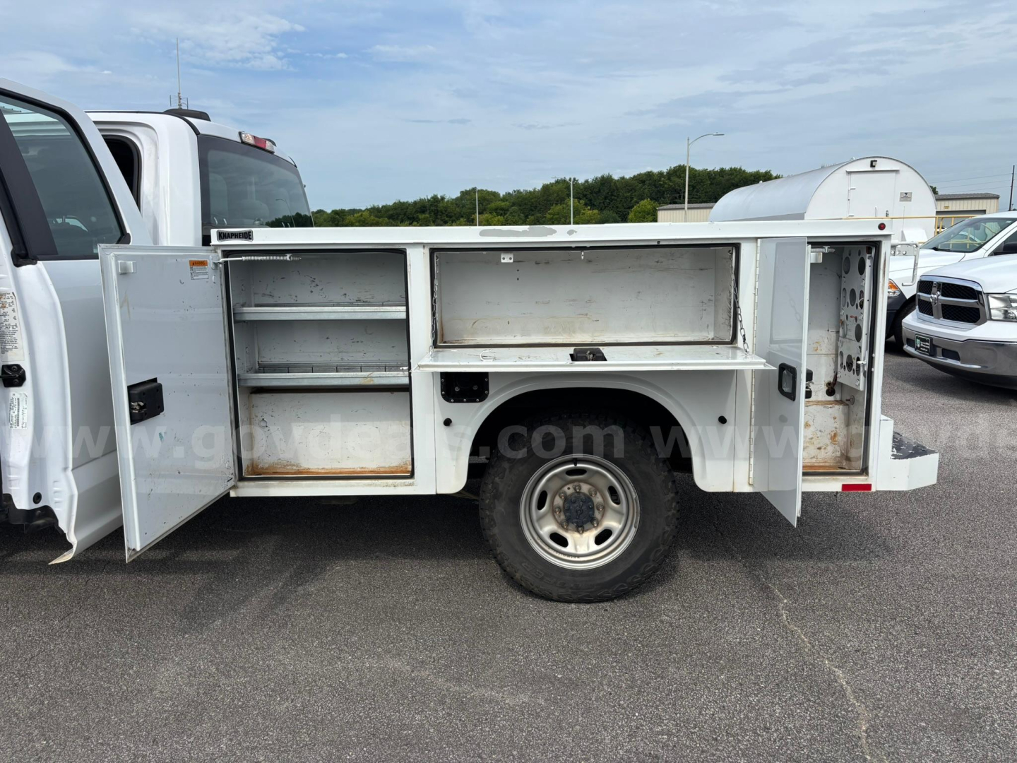 Truck service body side compartments open showing storage cabinets and shelves with metal doors.