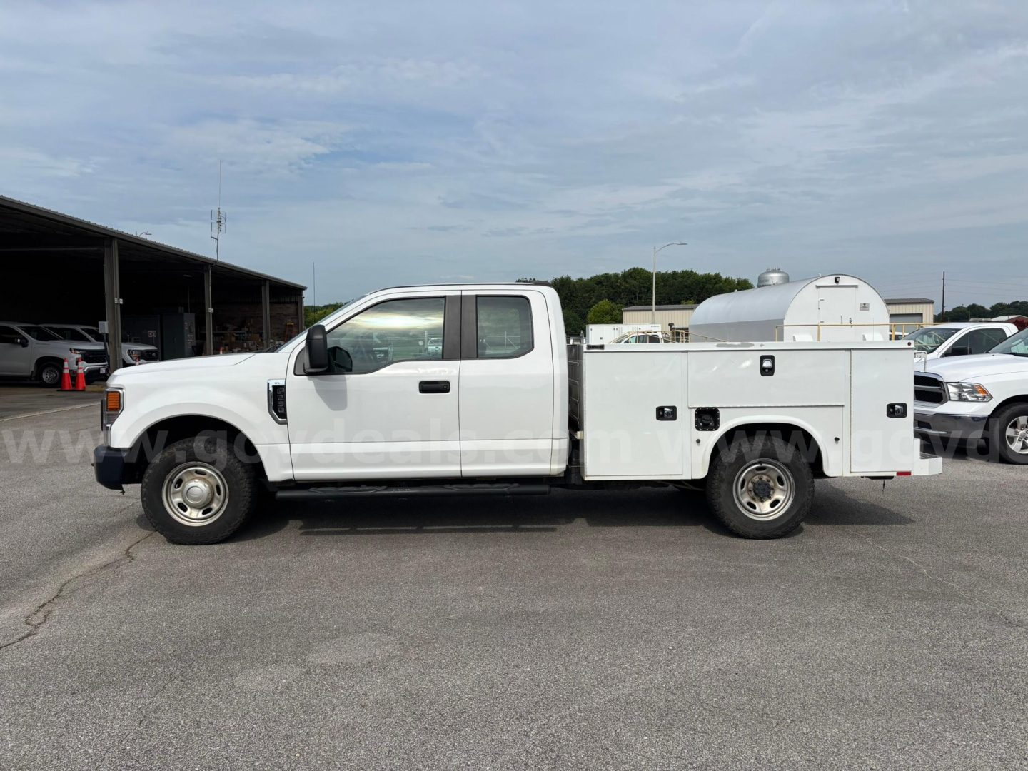 Side view of a white Ford F-250 utility service truck with a canister storage compartment in the bed. Visible text includes no readable labels on the truck side.