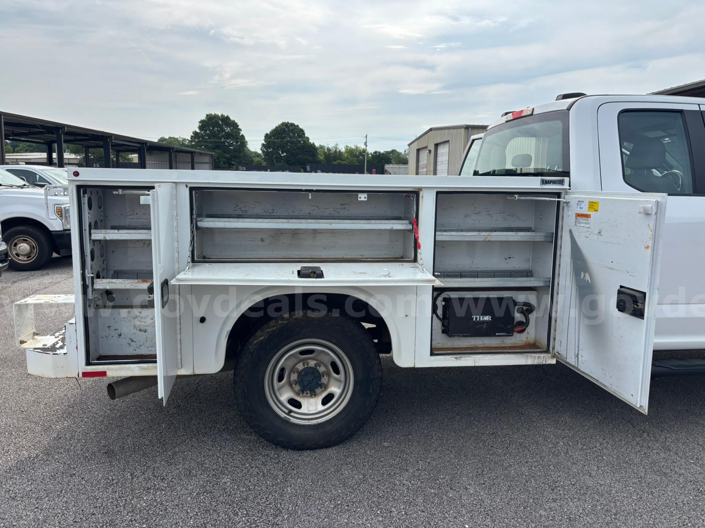 Service bed of a 2021 Ford F-250 utility truck showing side compartments and open doors with storage shelves and a toolbox.