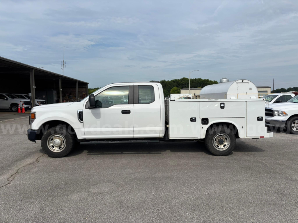 Side view of a white Ford F-250 utility service truck with a canister storage compartment in the bed. Visible text includes no readable labels on the truck side.