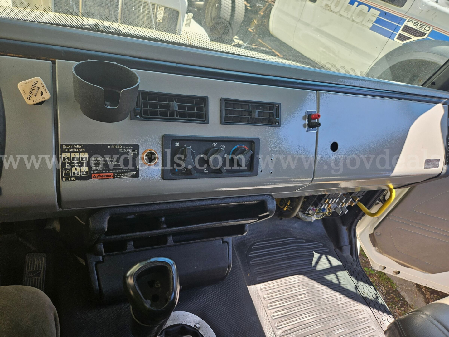 Truck cab interior dashboard of a Freightliner FL106 showing steering area, dashboard vents, cup holder, and dash sticker with controls.