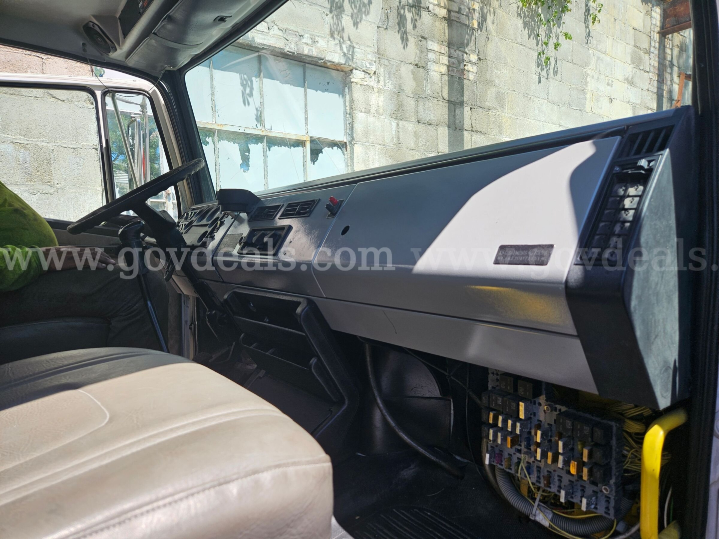 Dashboard of a Freightliner cab showing instrument cluster and glove compartment; interior view from passenger seat with wiring and fuse box visible.