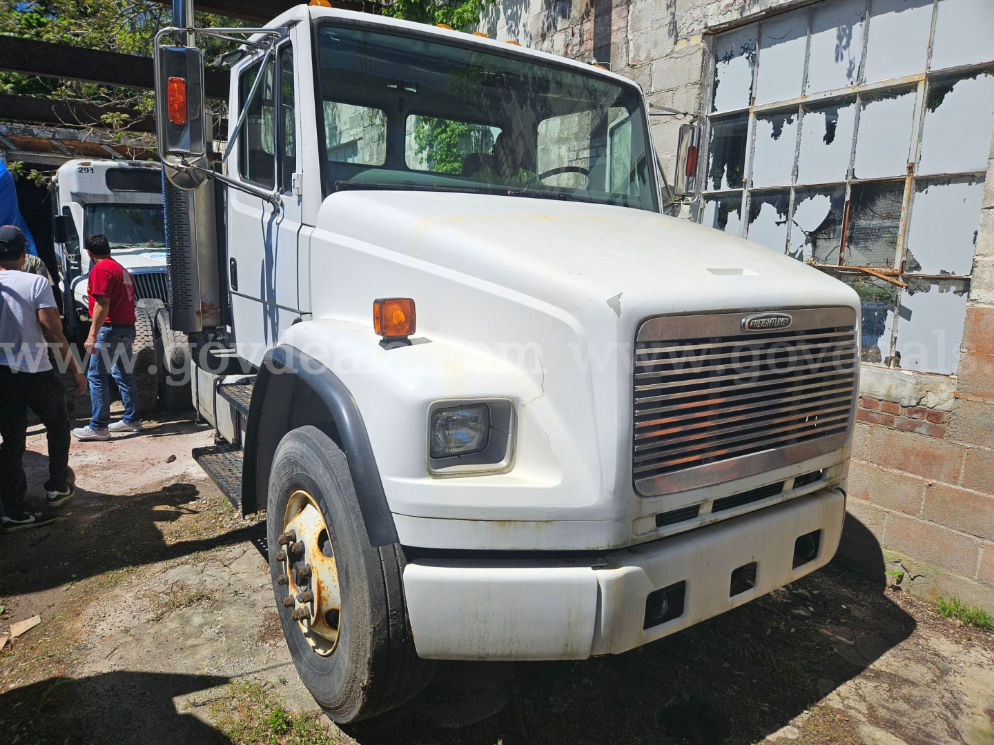 White Freightliner FL106 cab and chassis truck front view showing large grille, rectangular headlights, side mirrors, and a steel bumper with a few rust spots on the wheel hub.