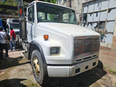 White Freightliner FL106 cab and chassis truck front view showing large grille, rectangular headlights, side mirrors, and a steel bumper with a few rust spots on the wheel hub.