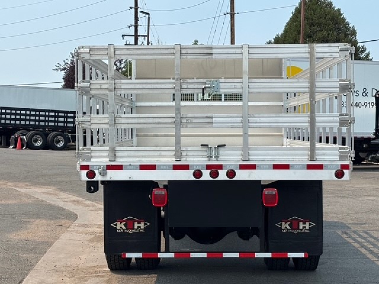 Mack MD7 flatbed truck rear view showing aluminum stake sides and dual rear red lights with black mud flaps and Kentucky Truck logo.