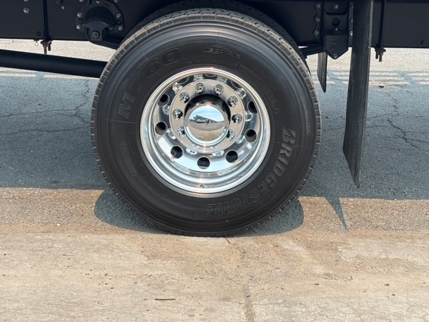 Wheel of new Mack MD7 flatbed truck showing polished steel rim and tire with tread, part of the chassis visible.