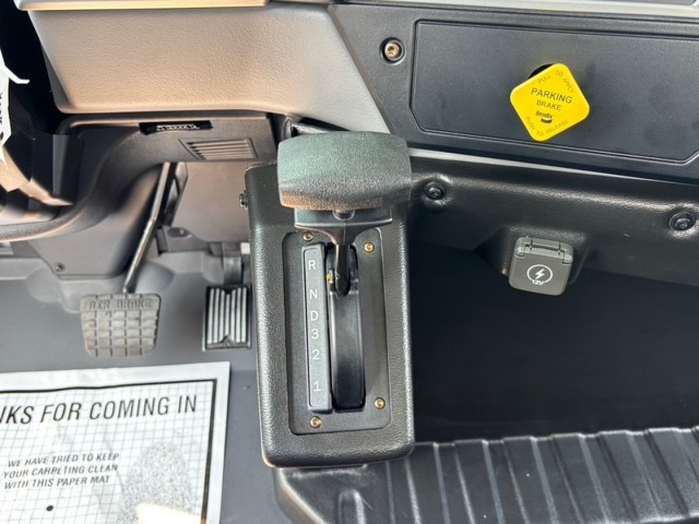 Cab interior showing automatic transmission gear selector with R N D 3 2 1, pedal area, and a yellow label on the dash.