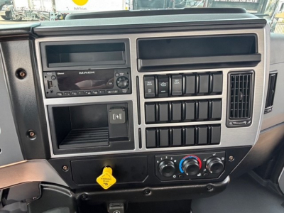 Dashboard of a 2026 Mack MD7 cab; visible features include a Mack radio unit, multiple control switches, circular climate controls, and a yellow parking brake knob.