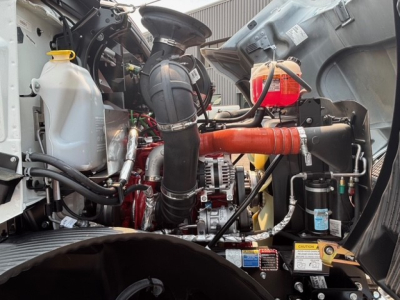 MD7 engine bay showing coolant reservoir, turbo intake, hoses, and alternator in a Mack truck. Visible components include coolant bottle, air intake hoses, orange hose, and electrical wiring.