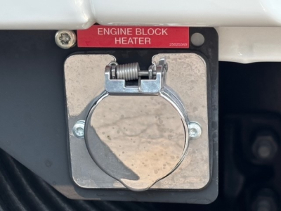 Engine block heater cover on Mack MD7 engine bay with red label reading ENGINE BLOCK HEATER