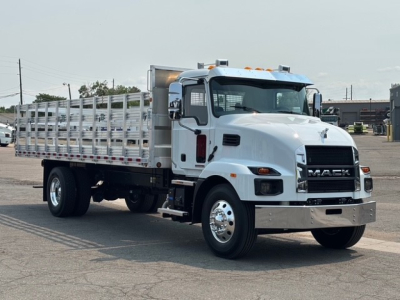 Mack MD7 flatbed truck in a light color, side profile view with aluminum stake bed, chrome front bumper, and dual rear wheels.