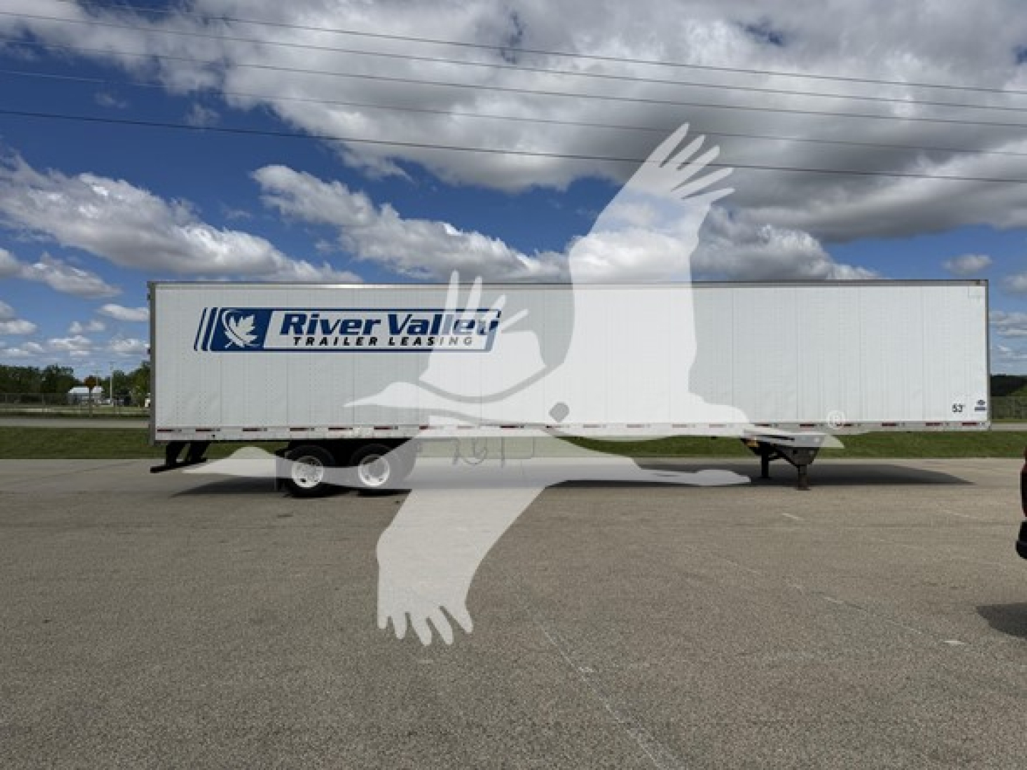 Trailer side view showing River Valley branding and a white utility trailer with dual axles, under a blue sky.