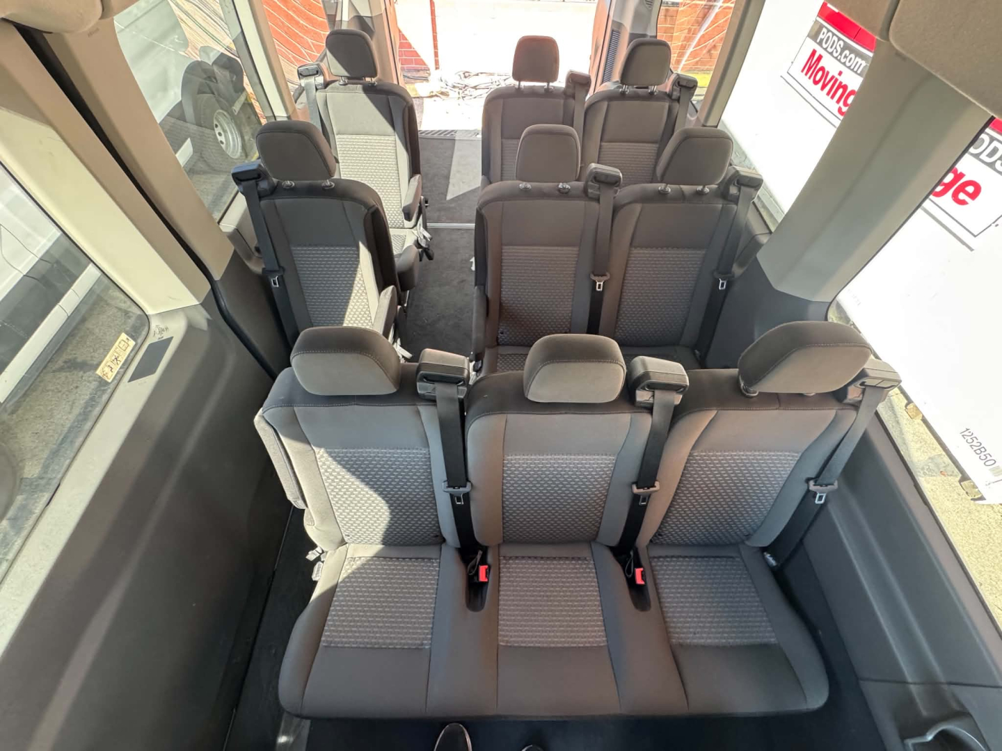 Ford Transit 350 HD interior showing multiple rows of seating in passenger van configuration with gray fabric seats and seat belts.