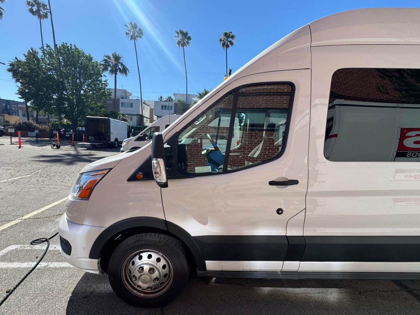 Ford Transit 350 HD van side view showing front door and passenger window, white exterior with black trim, wheel and side mirror visible.